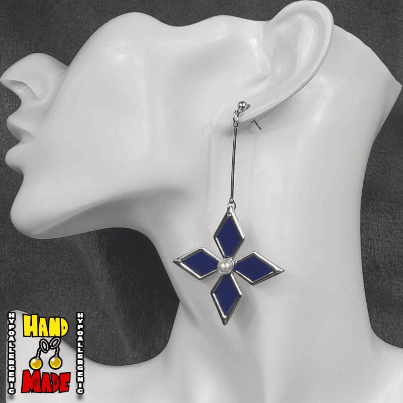 A pair of blue and silver flower earrings with a white pearl center displayed on a mannequin ear.