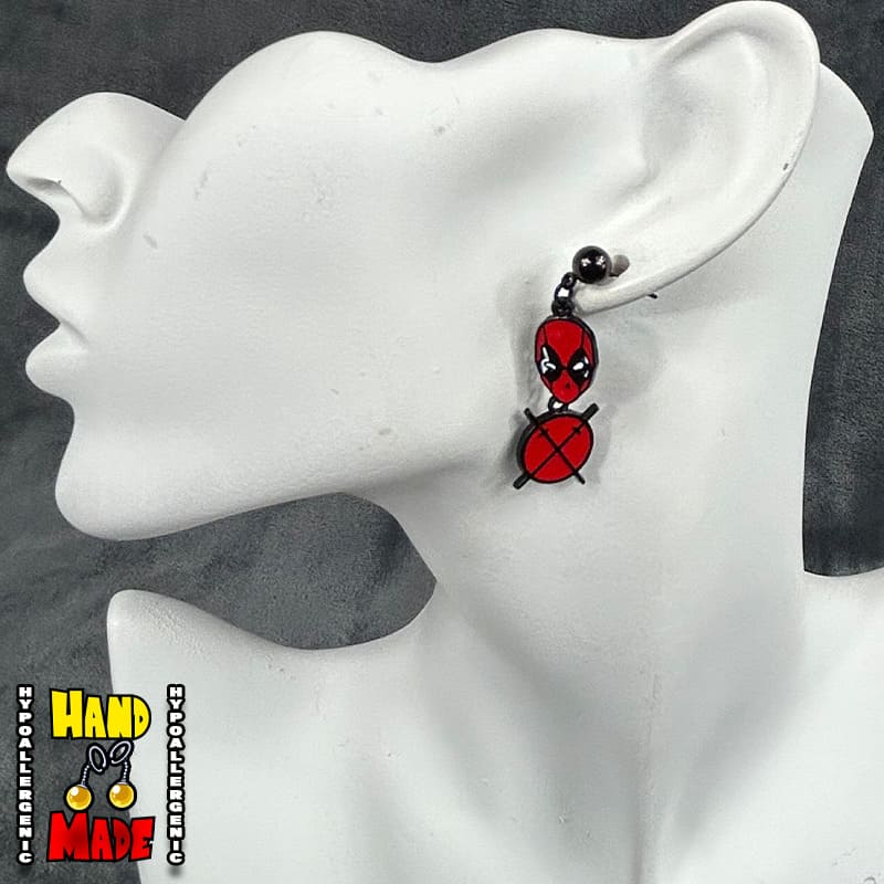 A pair of Deadpool-themed cross earrings displayed on a mannequin head, featuring the iconic character in red and black.