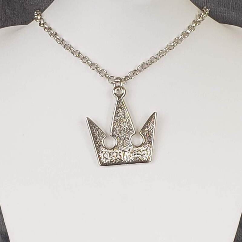 A silver-colored crown-shaped necklace on a mannequin bust, featuring a silver chain.